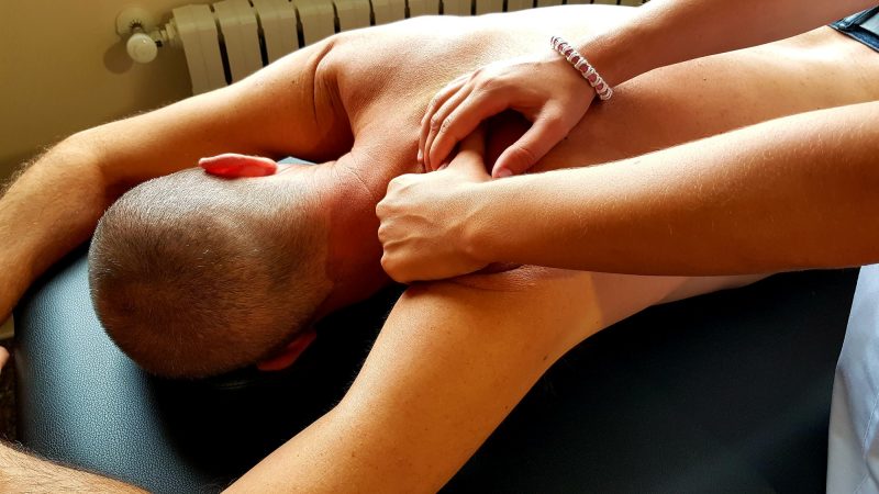 Female physical therapist assinting a male patient giving exercising treatment massaging the back